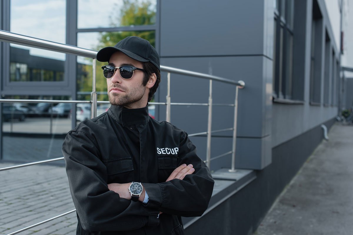 A security guard standing with his arms crossed in front of a grey