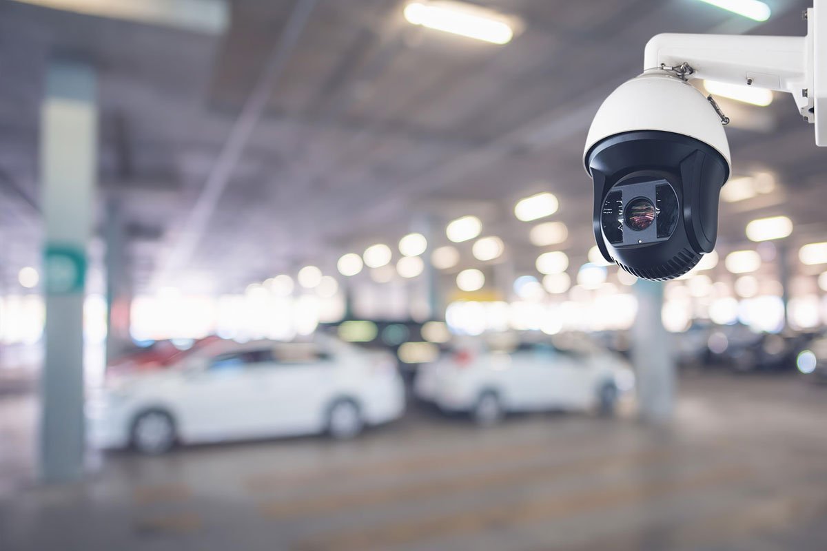 A modern security camera affixed to the ceiling in a dimly lit underground parking garage.