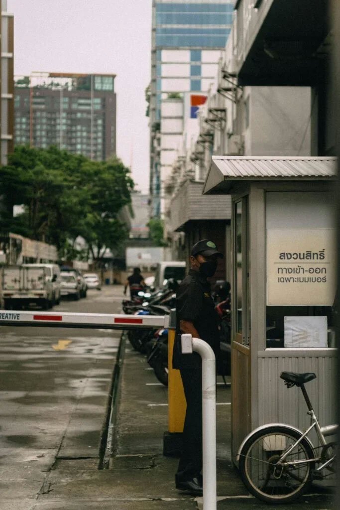 Security guard standing by a barrier gate and guard booth on a city street.