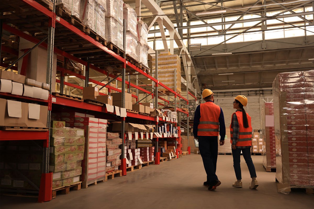 Two warehouse workers walking through a warehouse and inspecting items.